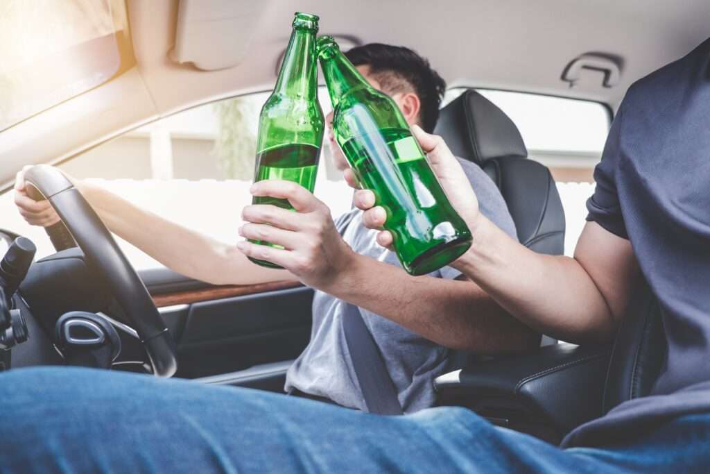 Two asian man drives a car with drunk a bottle of beer alcohol behind the steering wheel of a car