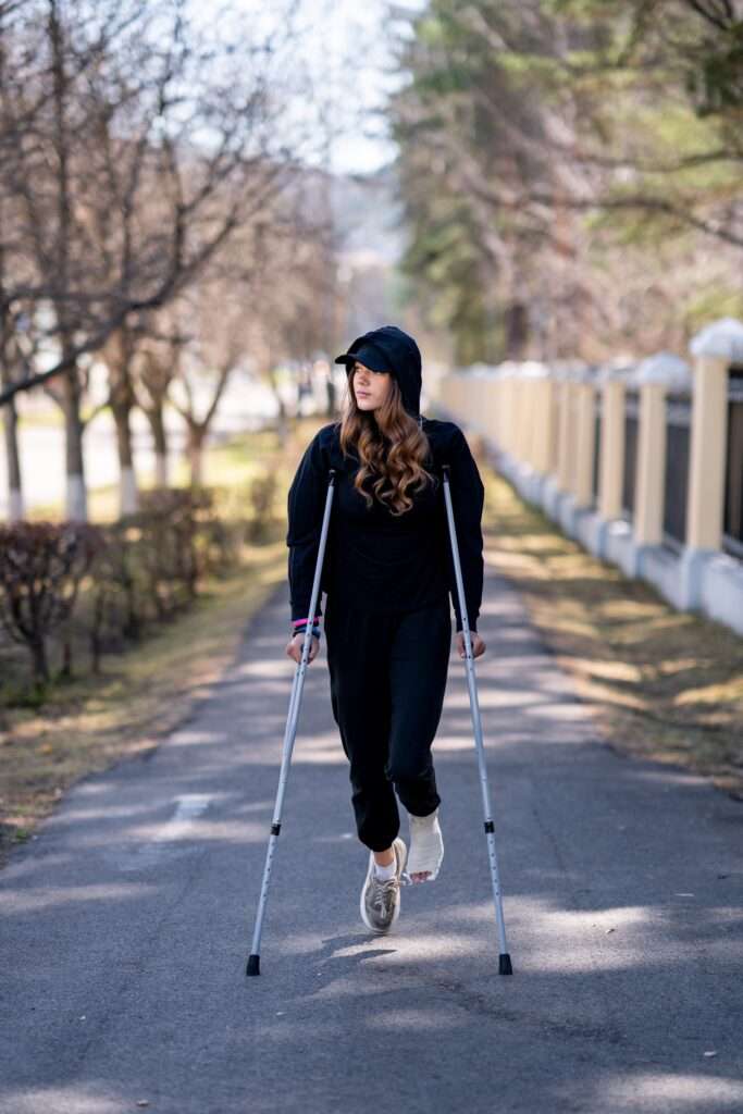 young woman with a broken ankle walks on road.